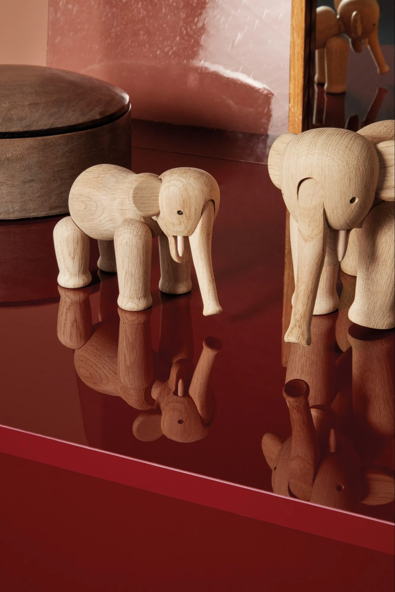 Two light wood elephant figurines standing on a reflective red surface.