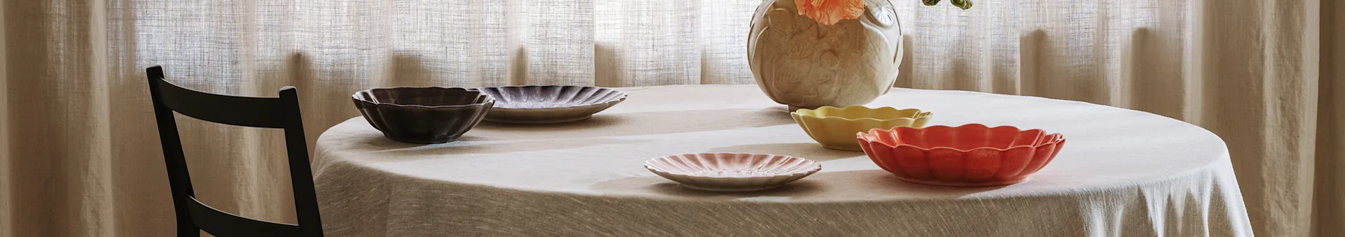 Fluted ceramic bowls and plates in various colors on a round table with a light tablecloth.