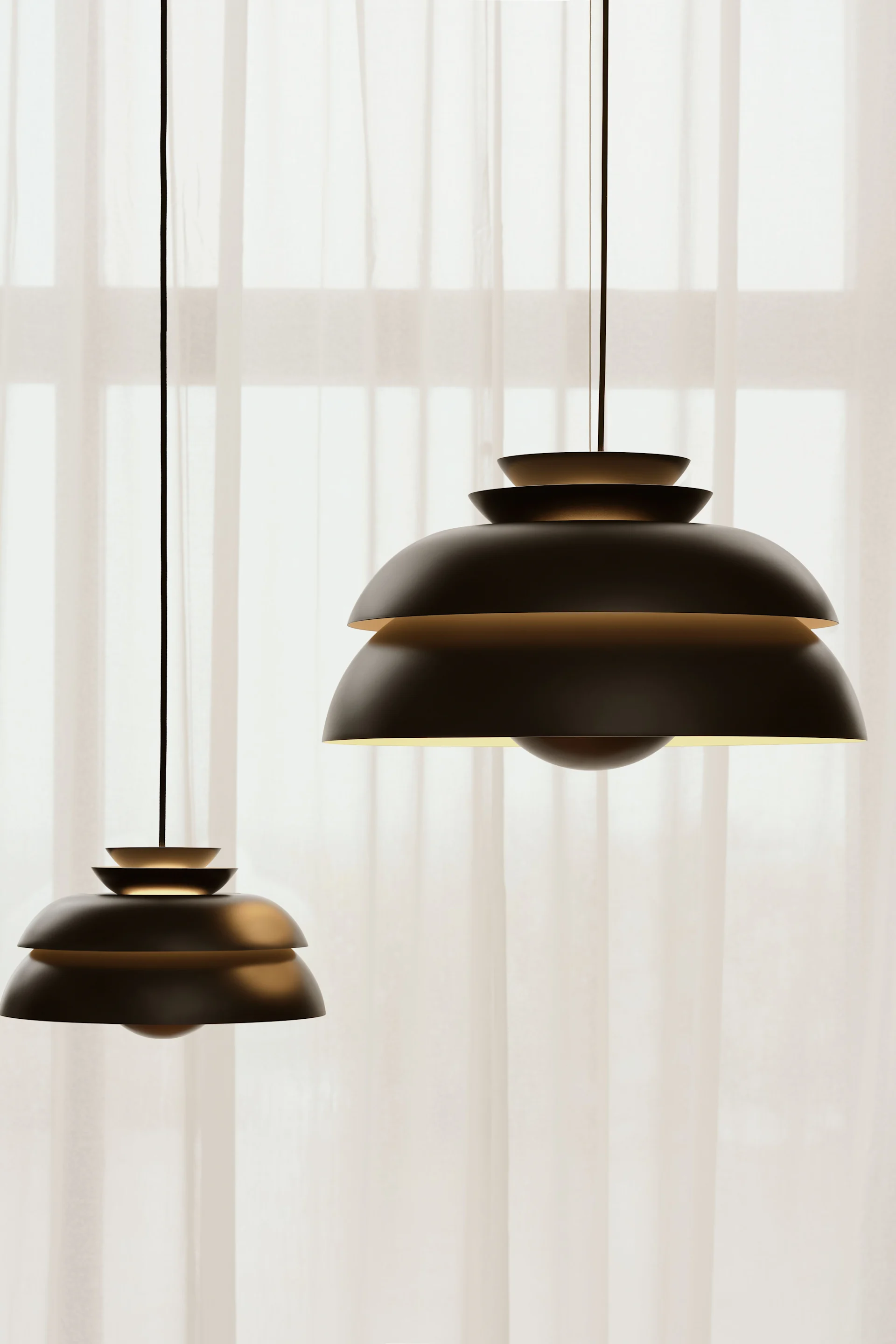 Two dark, layered pendant lamps emit a warm glow in front of sheer white curtains.