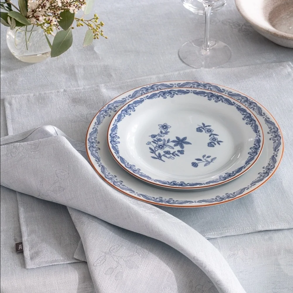 Stacked white plates with blue floral and ornate patterns, light blue placemat, and folded napkin on a table.