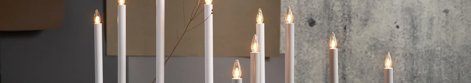 Close-up of several white electric candles with warm, flickering lights, some with a thin, dry branch intertwined.